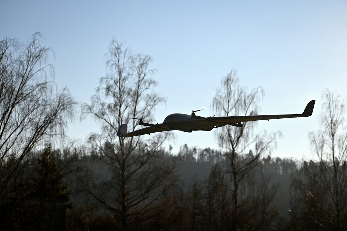 Fixed-wing survey drone in flight above treeline